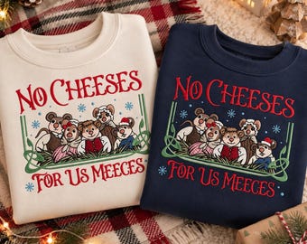 May include: Two crewneck sweatshirts, one cream and one navy blue, each featuring an embroidered graphic of five mice in winter clothing. The text reads NO CHEESES FOR US MEECES in red, framed by green decorative lines and small blue snowflakes.
