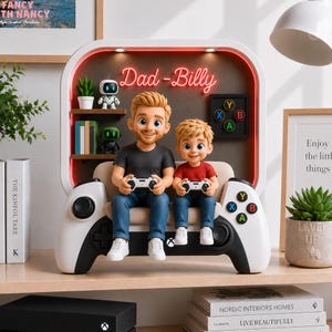 Könnte beinhalten: Dekorative Figur eines Vaters und Sohnes, die auf einer Couch in Form eines Gamecontrollers sitzen und jeweils einen Controller halten. Die Figur hat ein Regal mit kleinen Pflanzen und Robotern. Die Worte "Dad-Billy" sind in rotem Neon.