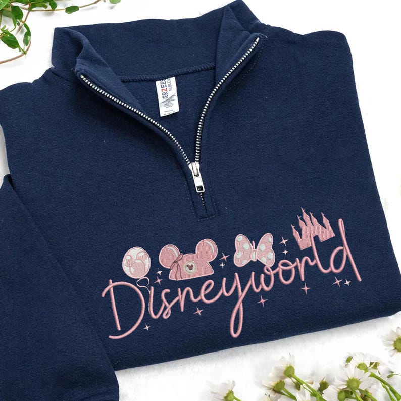 May include: Navy blue quarter-zip sweatshirt with a pink embroidered "Disneyworld" design. The design includes a castle, balloons, and Mickey Mouse-themed elements. The sweatshirt has a silver zipper and a tag.