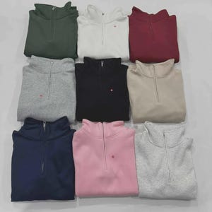 May include: Nine quarter-zip sweatshirts in various colors, including green, white, burgundy, gray, black, beige, navy, pink, and light gray. Each sweatshirt has a small red logo near the zipper.
