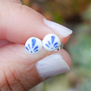 May include: A pair of white ceramic stud earrings with a blue floral design.