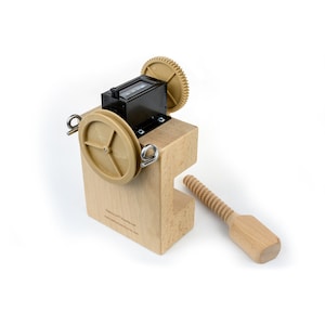 Könnte beinhalten: Ein Holzgerät mit einem schwarzen Zähler und zwei Zahnrädern. Das Gerät ist auf einem Holzsockel montiert, an dem ein Holzgriff an einer Schraube befestigt ist. Das Gerät dient zum Zählen.