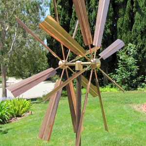 May include: A copper wind spinner with multiple blades, rotating in the wind. The blades are arranged in a starburst pattern and are attached to a central hub. The spinner is mounted on a tall metal pole.
