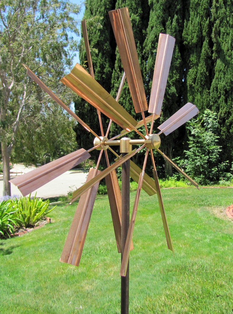 May include: A copper wind spinner with multiple blades, rotating in the wind. The blades are arranged in a starburst pattern and are attached to a central hub. The spinner is mounted on a tall metal pole.
