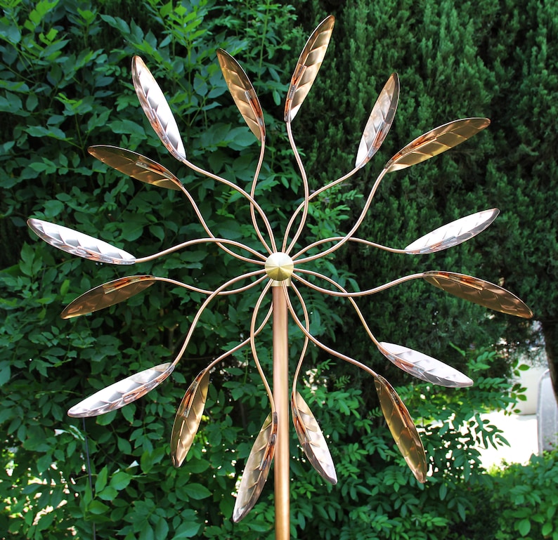 May include: A copper wind spinner with multiple leaves that spin in the wind. The leaves are arranged in a circular pattern around a central pole. The wind spinner is a decorative garden ornament.
