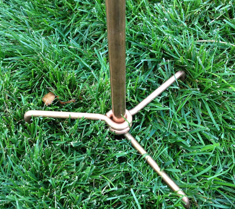 May include: A copper metal stand with three legs. The stand is designed to be inserted into the ground.