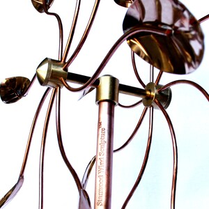 May include: A copper wind sculpture with multiple arms and leaves. The sculpture is mounted on a copper pole with the text "Stanwood Wind Sculpture&trade;" engraved on the pole.