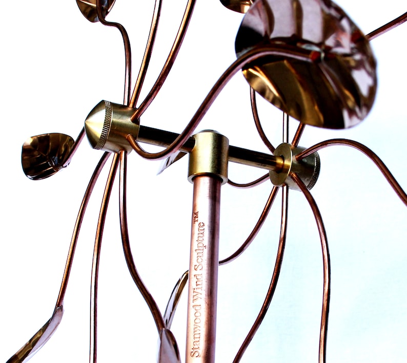 May include: A copper wind sculpture with multiple arms and leaves. The sculpture is mounted on a copper pole with the text "Stanwood Wind Sculpture&trade;" engraved on the pole.