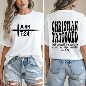 May include: White t-shirt with black text and a cross design. The front of the shirt reads "JOHN 7:24". The back of the shirt says "CHRISTIAN TATTOOED" with the text "look beneath the surface so you can judge correctly john 7:24".