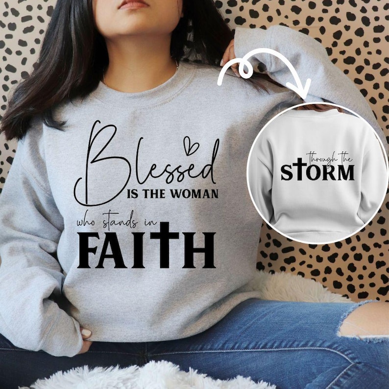 May include: A light gray sweatshirt with the words "Blessed is the woman who stands in Faith" in black script. A smaller image shows a white sweatshirt with the words "through the STORM". The sweatshirt is a casual, comfortable style.