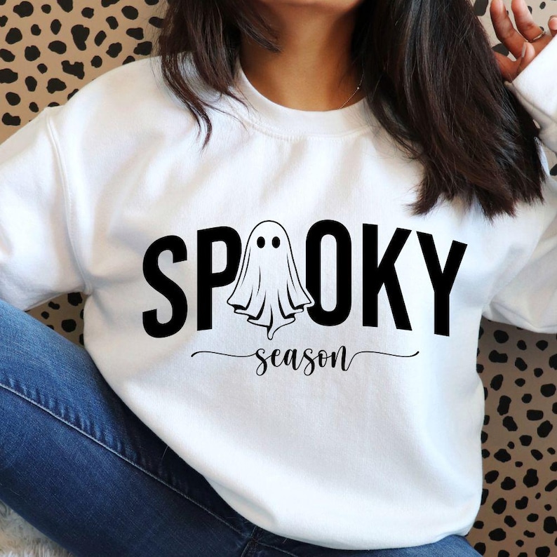 K&ouml;nnte beinhalten: Wei&szlig;es Sweatshirt mit den schwarzen Worten "SPOOKY season" und einer Geistergrafik. Das Design ist mittig auf der Vorderseite des Sweatshirts platziert. Das Sweatshirt ist aus weichem Material.