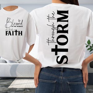 May include: White t-shirt with black text. The front of the shirt says "Blessed is the woman who stands in Faith." The back of the shirt says "Through the STORM."