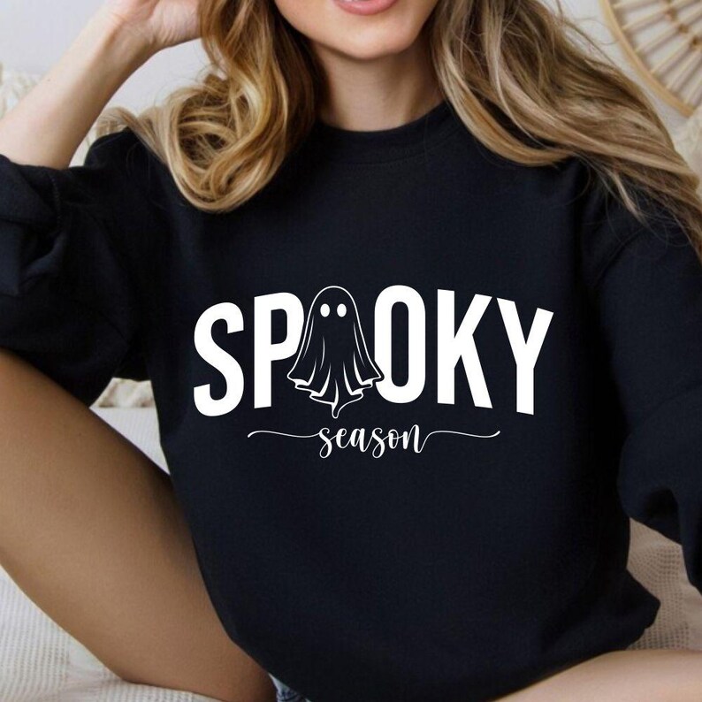 K&ouml;nnte beinhalten: Schwarzes Sweatshirt mit den wei&szlig;en Worten "SPOOKY season" und einer Geistergrafik. Das Design befindet sich mittig auf der Vorderseite des lang&auml;rmeligen Oberteils. Das Sweatshirt ist ein l&auml;ssiges Kleidungsst&uuml;ck, perfekt f&uuml;r Halloween.
