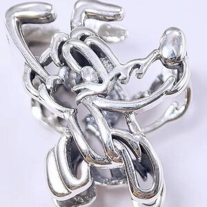 May include: A silver ring with an abstract design. The ring has intertwined, curved shapes and a polished finish. The design is intricate and appears to be made of a durable metal.