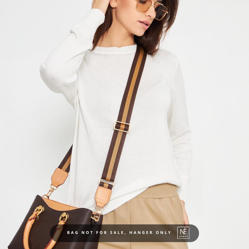 May include: A brown handbag with a striped shoulder strap featuring tan and gold stripes. The bag has gold-coloured hardware and a tan leather handle. The text "BAG NOT FOR SALE, HANGER ONLY" is visible at the bottom.