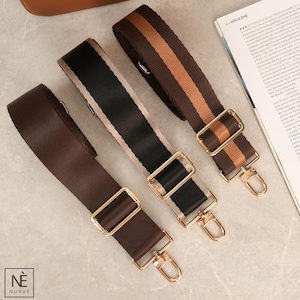 Peut inclure: Trois bandoulières de sac réglables, dans les tons marron, noir et beige, chacune avec une quincaillerie métallique dorée. Une sangle présente un motif à rayures marron et beige. Les sangles sont présentées sur une surface claire.