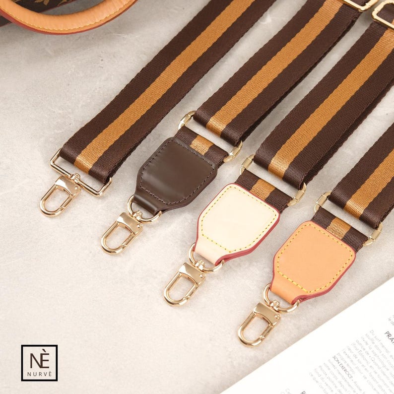 May include: Four brown and gold striped bag straps with gold-coloured metal fixings. Each strap features a different coloured leather accent: brown, cream, and peach. These straps are designed for handbags.