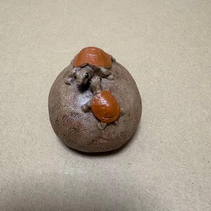 May include: A brown, textured sculpture of a rounded rock with three turtles. Two turtles have orange shells and are positioned on top of the rock. The third turtle is smaller and has a brown shell.