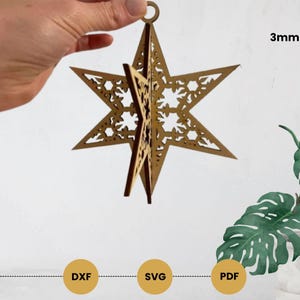 Könnte beinhalten: Ein lasergeschnittener Holzstern-Ornament mit filigranen floralen Mustern. Der Stern wird von einer Hand gehalten, was sein dreidimensionales Design zeigt. Das Ornament ist etwa 3 mm dick und hat eine kleine Schlaufe zum Aufhängen. Der Text "DXF", "SVG" und "PDF" ist ebenfalls zu sehen.