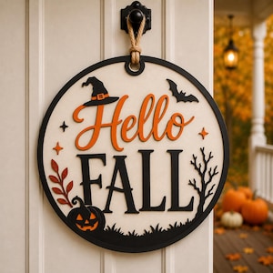 May include: A circular wooden door sign featuring the text Hello FALL in orange and black. The design includes a black witch hat, a flying bat, a jack-o'-lantern, a bare tree, and orange leaves. It hangs from a black hook by a thick jute rope.