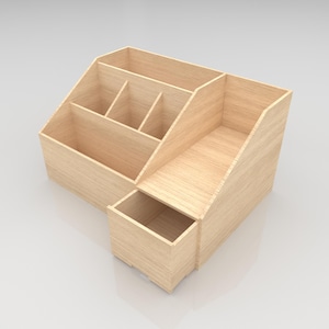 May include: A light-colored wooden desk organizer with multiple compartments. The organizer has a rectangular shape with angled sides and a small drawer. It features several open sections for storing office supplies.