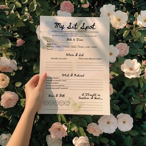May include: A white paper titled "My Sit Spot" is held in front of a backdrop of roses. The paper has prompts for recording observations in nature, including date, time, weather, and sensory details. The paper is surrounded by pink and white roses.