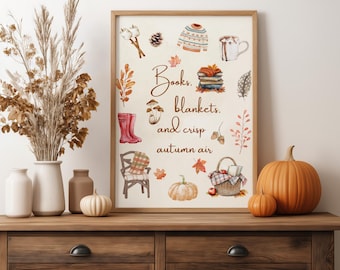 May include: A framed print with an autumn theme, featuring watercolor illustrations of fall items like pumpkins, a sweater, and boots. The text reads "Books, blankets, and crisp autumn air." The print is displayed on a wooden cabinet with vases and pumpkins.