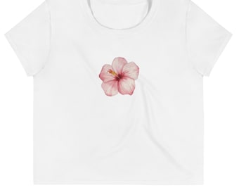 May include: White crop top featuring a watercolor hibiscus flower in shades of pink and yellow. The flower is centered on the front of the shirt. The top has a scoop neck and short sleeves.