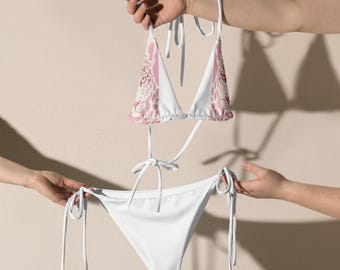 Könnte beinhalten: Ein zweiteiliges Bikini-Set. Das Oberteil hat einen rosa-weißen Animal-Print, während das Unterteil einfarbig weiß ist. Der Bikini wird von weißen Trägern und Bindebändern gehalten.