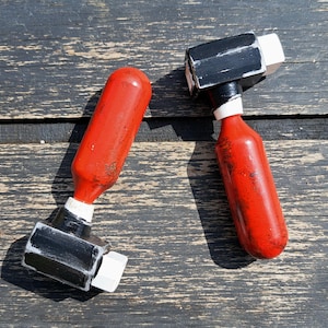 May include: Two red and black toy hammers with white accents. The hammers are made of wood and have a rounded head.