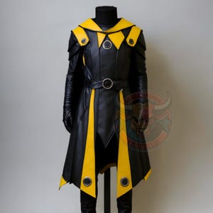 Puede incluir: Un disfraz de cuero negro y amarillo exhibido en un maniquí. El disfraz presenta un abrigo largo con detalles amarillos, un cinturón y detalles en los hombros. El diseño incluye adornos metálicos circulares y un cuello alto.