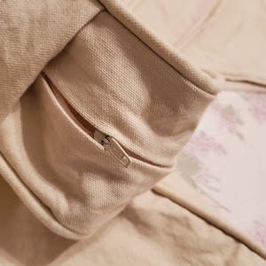 May include: A close-up of a cream-colored zipper on a fabric cushion. The zipper is partially open, revealing a floral pattern on the inside of the cushion.