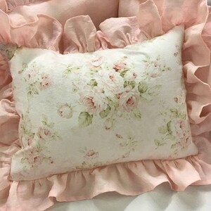 May include: A pink pillow with a white floral print and ruffled edges. The pillow is made of soft fabric and has a delicate, feminine look.