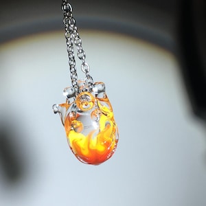 Op de afbeelding: Een glazen hartketting met een heldere glazen hart hanger met een geel en oranje vlamontwerp.