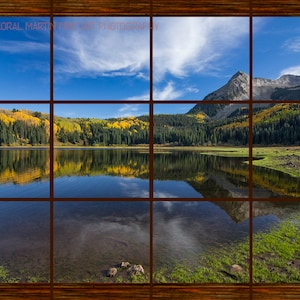 May include: A scenic view of a lake with a mountain in the background. The lake is surrounded by trees with yellow leaves. The sky is blue with white clouds. The image is framed in a wooden window.