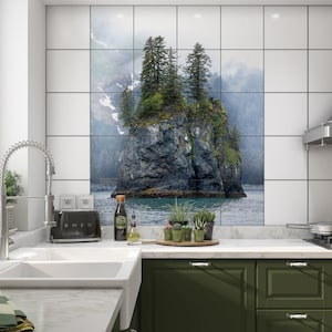 May include: A kitchen with white tile backsplash featuring a scenic image of a rocky island with green trees and a blue body of water. The kitchen has a stainless steel sink, faucet, and a black toaster. There are green cabinets below the counter.