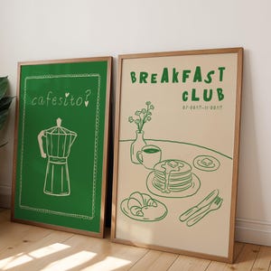 May include: Two framed art prints. One features a green background with a white coffee maker illustration and the text "cafesito?". The other print has a beige background with a green illustration of breakfast items and the text "BREAKFAST CLUB".