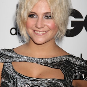 May include: A smiling woman with short, blonde hair is wearing a black dress adorned with silver sequins. The dress features a keyhole neckline and a patterned design. The background includes the letters "GQ" and the word "LONDON".