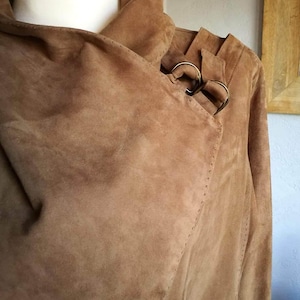 May include: A brown suede jacket with a long collar and a buckle detail on the shoulder.