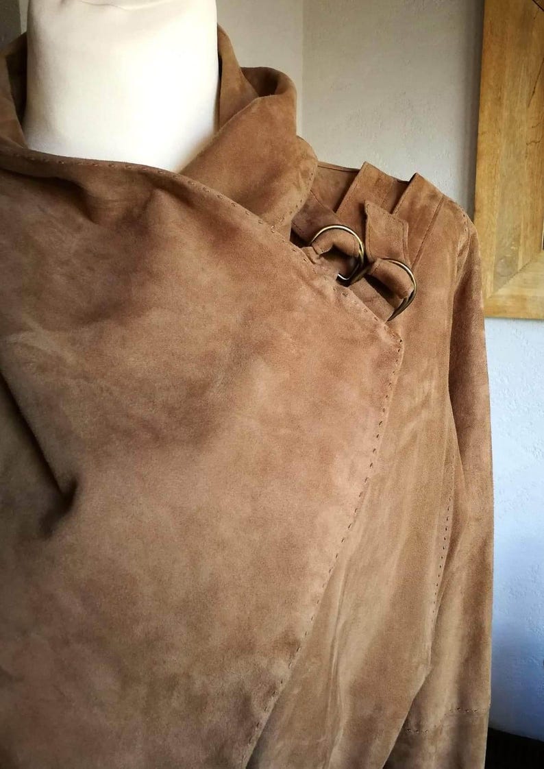 May include: A brown suede jacket with a long collar and a buckle detail on the shoulder.
