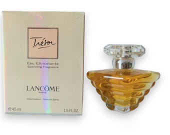 Puede incluir: Un frasco de perfume Lancôme Trésor Eau Étincelante Sparkling Fragrance de vidrio transparente. El frasco tiene forma de diamante y contiene un líquido de color dorado. La caja es blanca con letras doradas y las palabras "Trésor", "Eau Étincelante", "Sparkling Fragrance", "Lancôme Paris", "Vaporisateur - Natural Spray", "e 45 ml" y "1.5 FL. OZ."