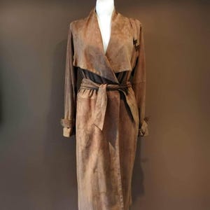 May include: A long brown suede coat with a wrap style collar and a tie belt.