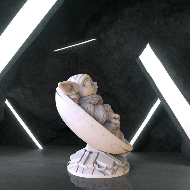 May include: A white ceramic figurine of a character from the Star Wars franchise, sitting in a pod-like chair. The figurine is on a white base with a textured surface.