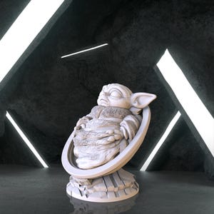 May include: A white ceramic figurine of a sleeping baby Yoda, also known as Grogu, from the Star Wars series The Mandalorian. The figurine is in a seated position with its arms crossed and eyes closed. The figurine is on a circular base with a textured surface.