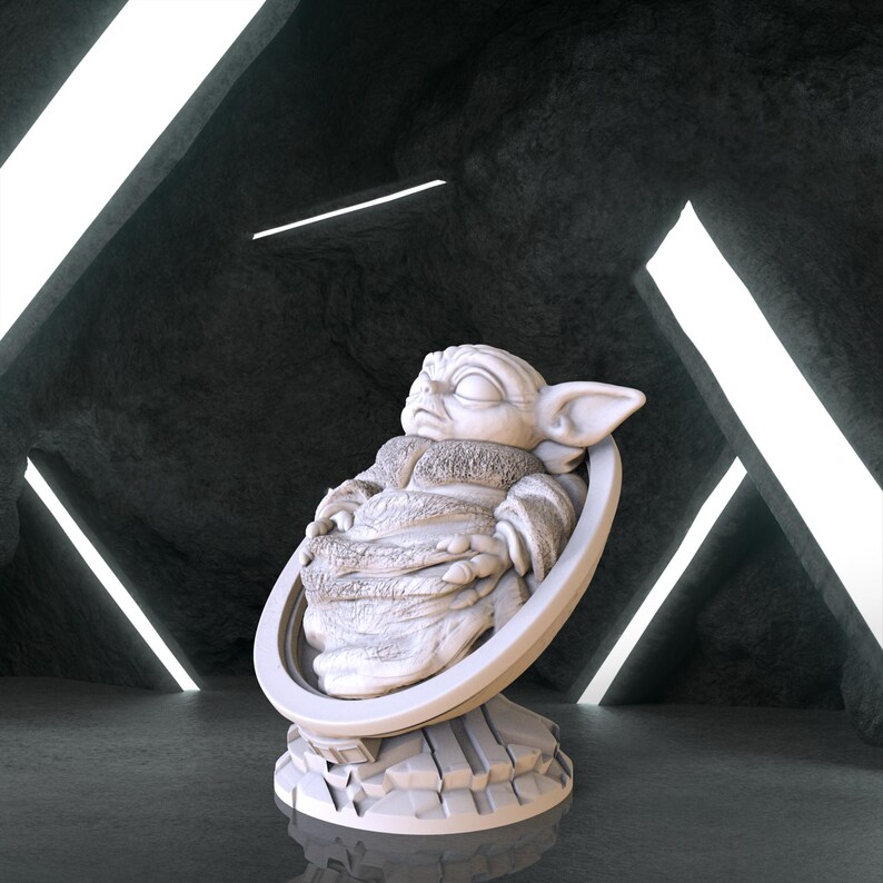 May include: A white ceramic figurine of a sleeping baby Yoda, also known as Grogu, from the Star Wars series The Mandalorian. The figurine is in a seated position with its arms crossed and eyes closed. The figurine is on a circular base with a textured surface.