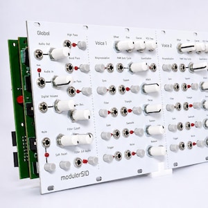 May include: A white modular synthesizer panel with numerous knobs, switches, and ports. The panel is labelled "modularSID" and features text such as "Global," "Voice 1," and "Voice 2." The panel has a green circuit board attached to the side.