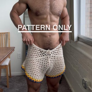 以下が含まれることがあります： クリーム色のクロシェ編みショートパンツ。ウエストはドローストリングで、青、黄、オレンジのカラフルなトリムが付いています。画像の上部には「PATTERN ONLY」というテキストが表示されています。このショートパンツは手作りのアイテムです。