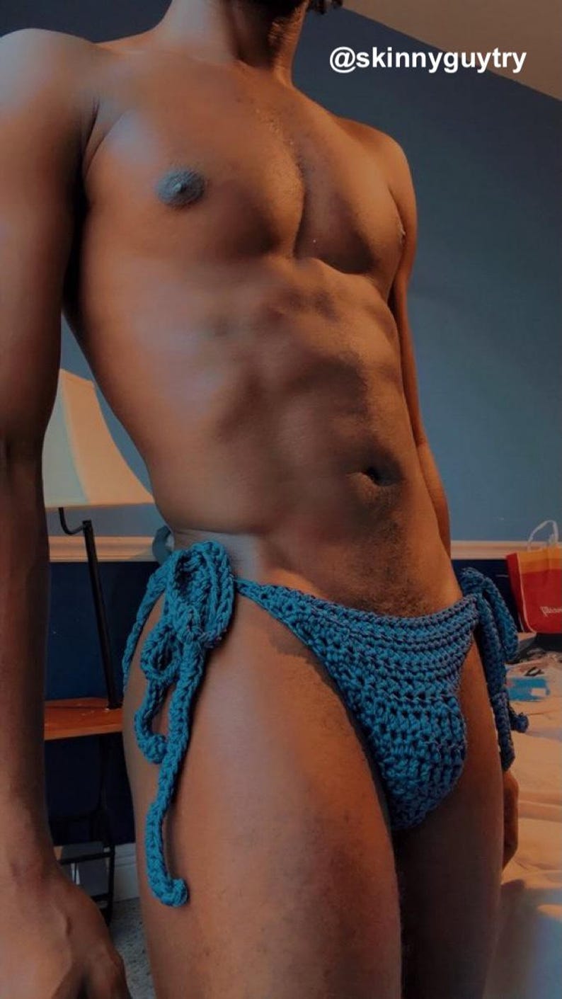 May include: A teal blue crochet bikini bottom featuring side ties with a textured knit pattern. The garment includes the text @skinnyguytry visible in the upper right corner of the frame. The piece is constructed with a visible yarn stitch.