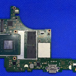 May include: A green circuit board featuring an array of electronic components, such as a processor, memory chips, and connectors. The board is rectangular with a curved edge, set against a blue backdrop. Components are in silver, black, and gold.