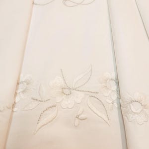 Peut inclure: Un textile en tissu blanc orné d'une broderie florale ton sur ton complexe avec des motifs de feuilles délicats et des bords festonnés. Le design comprend des détails cousus subtils et un motif botanique répétitif sur la surface.